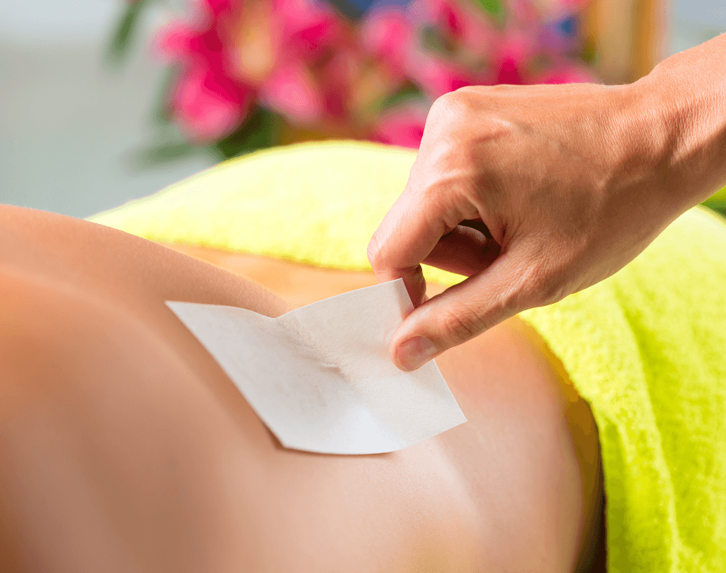 Close-up of a therapist’s hand removing a wax strip from a man’s back during a professional waxing treatment