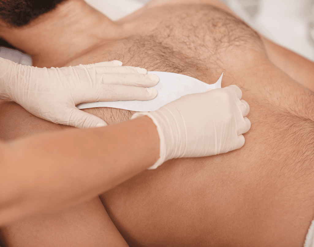 A close-up of a chest waxing treatment for men, showing a therapist wearing gloves applying a wax strip