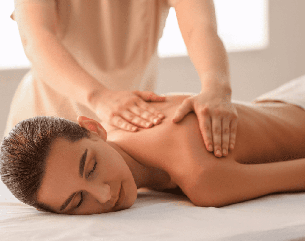 Woman lying face down receiving a back massage in a softly lit treatment room, creating a calm and therapeutic setting