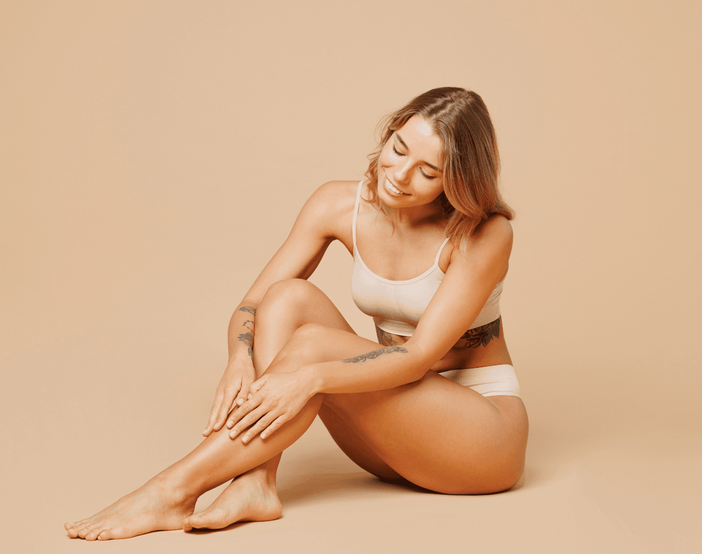 A smiling woman with smooth skin sitting comfortably, showcasing the results of a professional half leg and Brazilian wax treatment