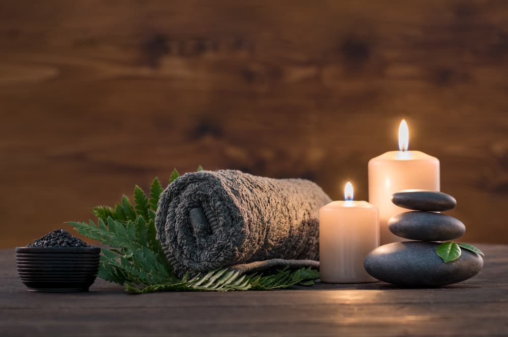 Rolled towel with spa stones, candles and green fern leaves on a wooden table, creating a calm and relaxing atmosphere at The Beauty Spot in Wadebridge.